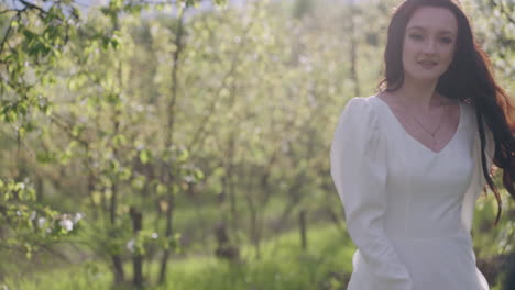 stunning-brunette-woman-in-white-dress-is-enjoying-walk-in-blooming-garden-whirling-between-trees